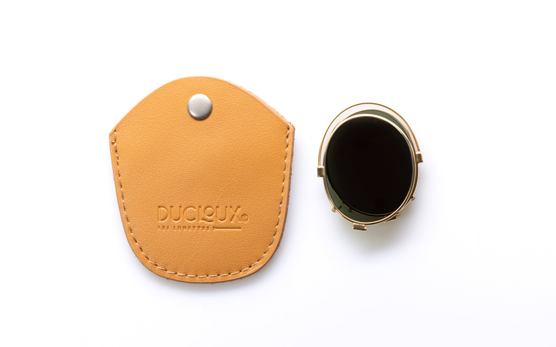 A tan leather protective case, shown next to the clip on, which has a gold-toned metal frame and a dark screen. The leather case features a snap button closure and the brand name 'DUCISUX' embossed on it, set against a clean white background.