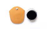 A close-up studio shot of a clip on with a black lens and silver bezel, shown next to its tan leather protective case on a white background. The case features the debossed brand name 'DUCLOUX'.