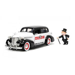 A diecast model of a classic 1939 black and white Monopoly car with red and white wheels, shown next to a miniature Sir Richard De Mille figurine on a white background.