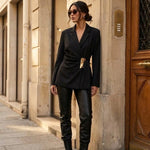 Model wearing KIDDING black tailored wrap blazer with notched lapels, structured shoulders, and self-tie waist belt with sculpted gold metal buckle paired with black leather pants