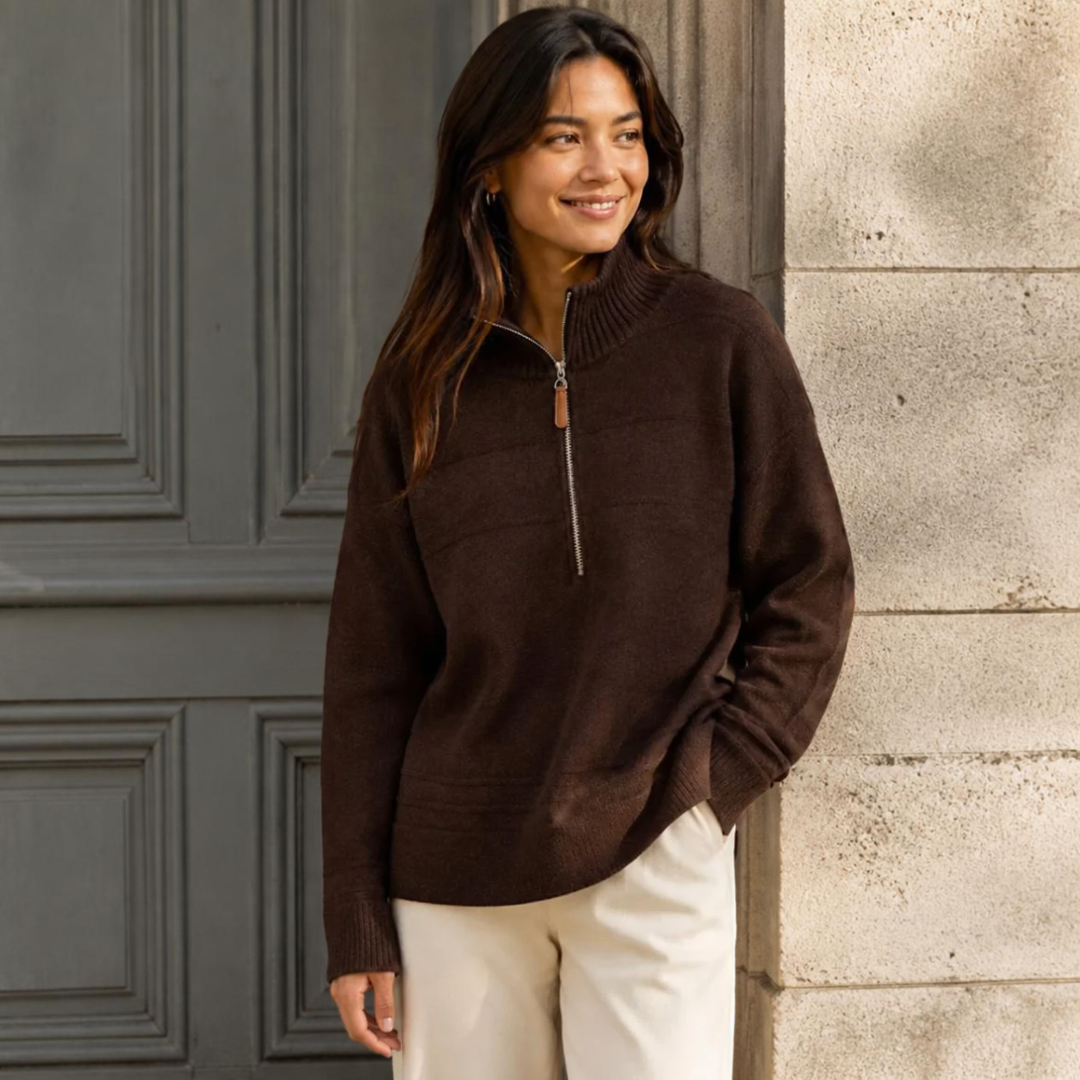 Model wearing KIDDING high-neck zip-up trucker sweater in dark chocolate brown with ribbed collar, cuffs, and hem, paired with cream trousers