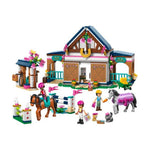 A toy building block set featuring a horse stable with a decorated roof, a small stable accessory area, a jumping fence, and several small minifigures with horses, shown on a plain white background.