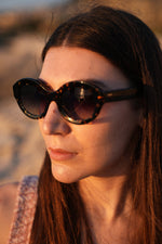 Side angle of a girl wearing tortoiseshell sunglasses and looking at the sunset. 