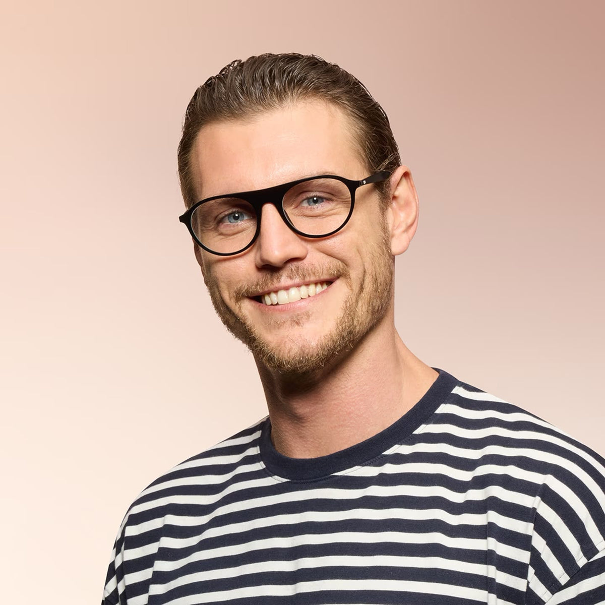 A man wearing black framed eyeglasses and black striped shirt on a pink background. 