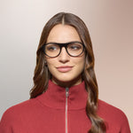 A woman wearing black framed eyeglasses and a red blouse on a pink background. 