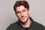 A man earing eyeglasses on a purple background. 