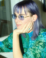 Side angle of a woman wearing gold framed sunglasses with blue lenses.