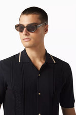 Side angle of a man wearing sunglasses with dark lenses on a white background. 