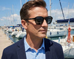 Side angle of a man wearing black sunglasses and a blue blazer. 