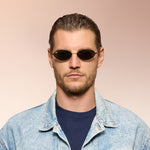 Front angle of a man wearing black sunglasses on a pink background. 