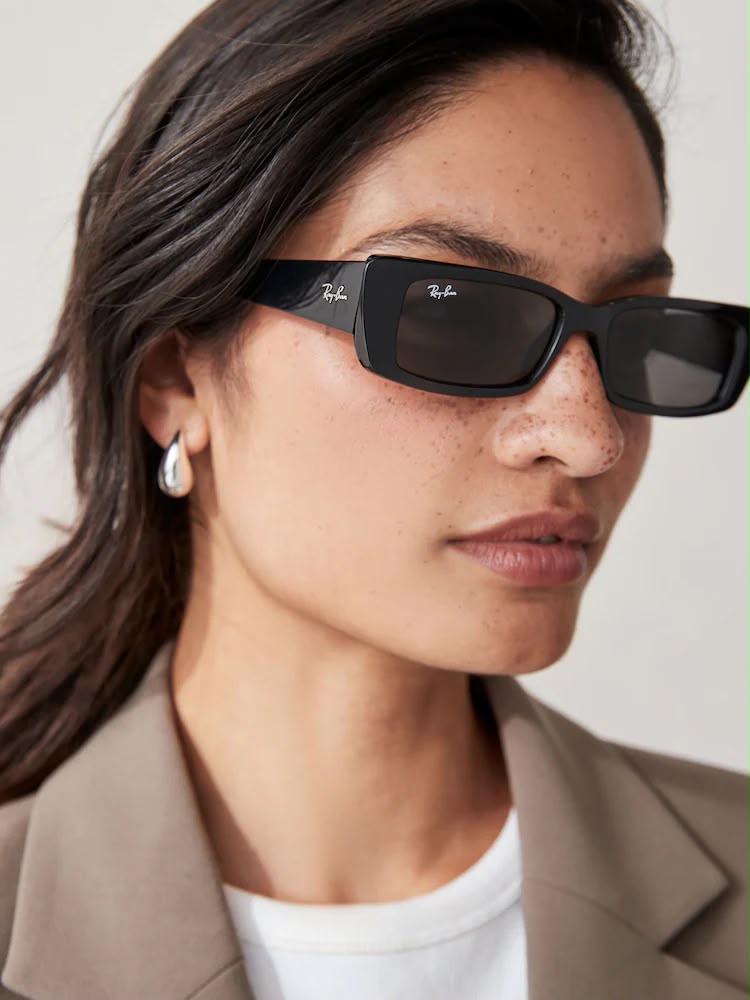 Side angle of a woman wearing black sunglasses with dark lenses on a white background. 