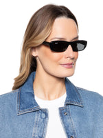 Side angle of a woman wearing black sunglasses on a white background. 