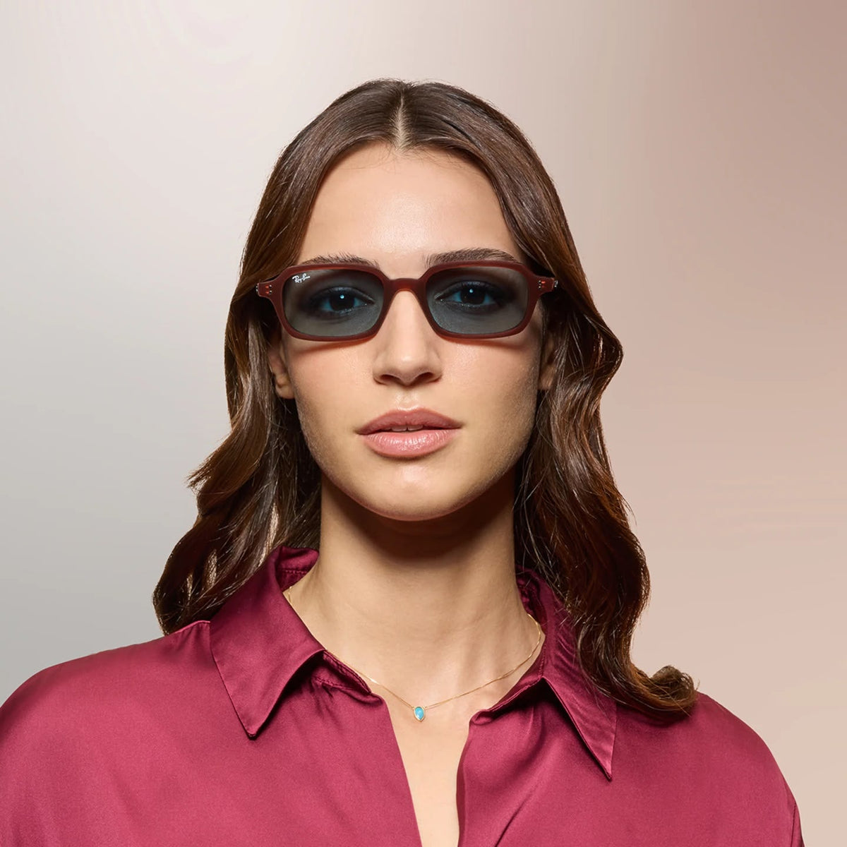 A woman wearing sunglasses and a pink blouse on a pink background.