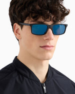 Side angle of a man wearing black sunglasses with blue lenses on a white background. 