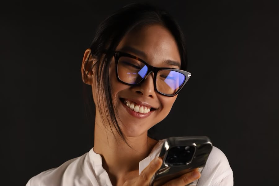 A girl wearing tortoiseshell eyeglasses on a dark background. 
