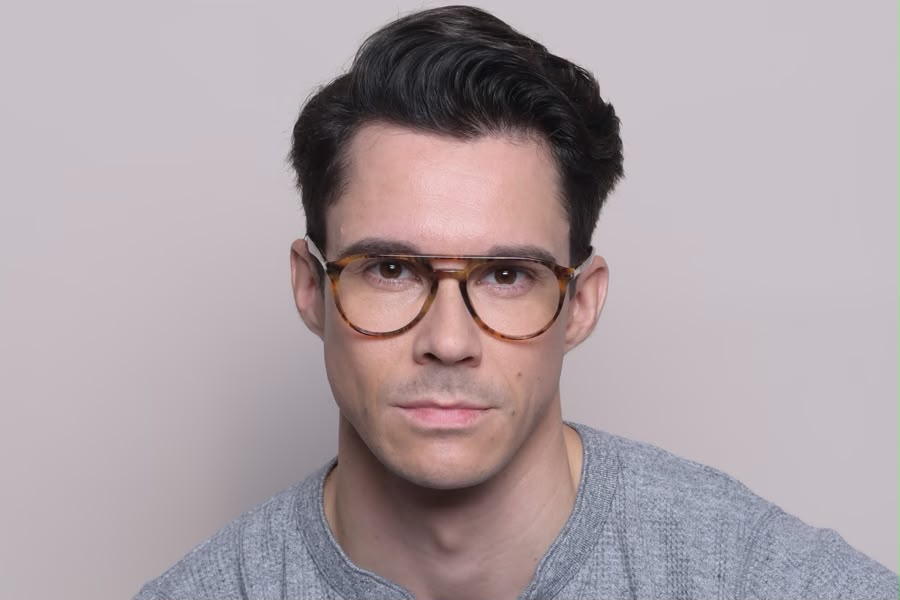 Font angle of a mean wearing tortoiseshell framed eyeglasses with a double bridge on a light grey background. 