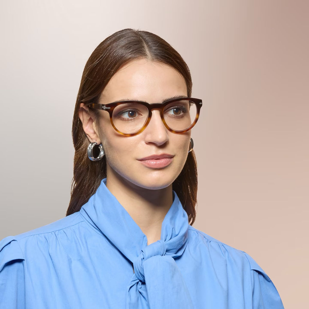 A woman wearing tortoiseshell eyeglasses on a pink background. 