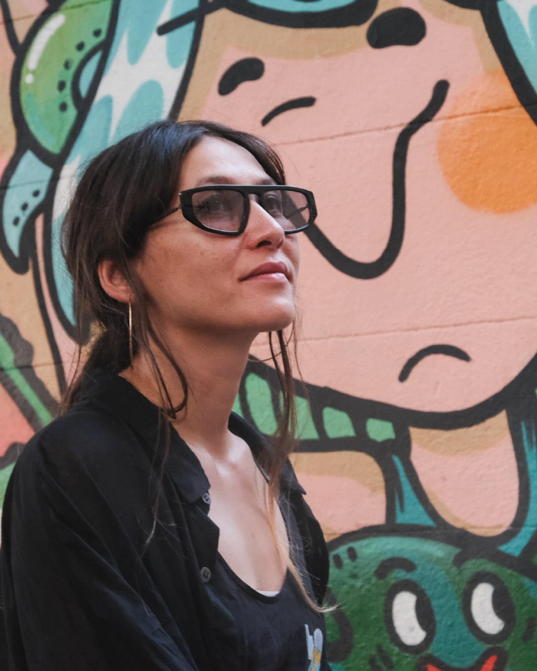Side angle of a woman wearing dark framed sunglasses on a colorful background.