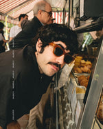Side angle of a man wearing orange framed sunglasses iwth dark lenses.