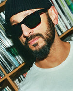 A man wearing tortoiseshell framed sunglasses and a white t-shirt. 