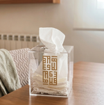 Clear tissue box with gold design on a wooden table in a home setting